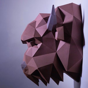 Puede incluir: Una escultura de papel marrón de una cabeza de bisonte, con un diseño geométrico. La escultura está montada en una pared blanca.