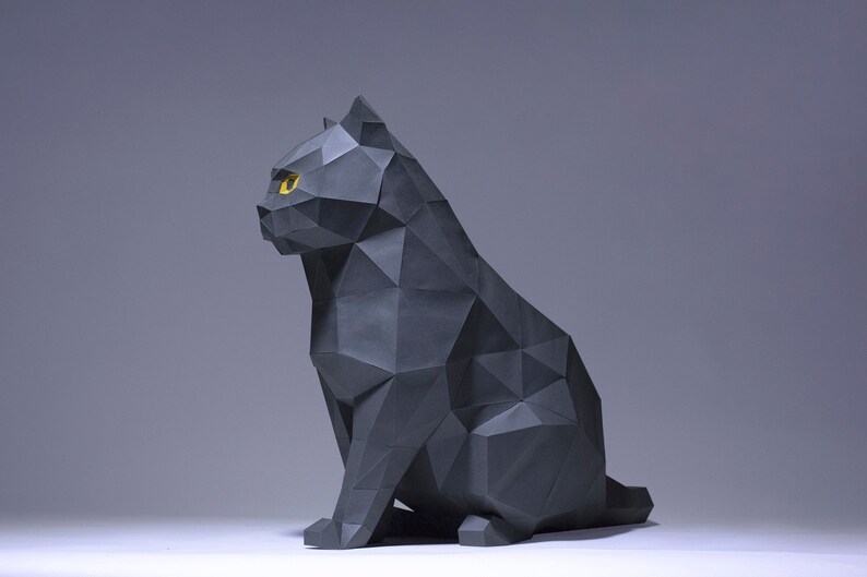 Pode incluir: Uma escultura de gato de origami preto com olhos amarelos. O gato est&aacute; sentado com a cabe&ccedil;a virada para o lado e a cauda enrolada ao redor do corpo.