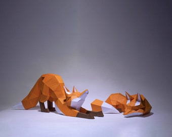 Puede incluir: Dos zorros de origami hechos de papel, uno naranja y blanco, el otro naranja y blanco, tumbados sobre una superficie blanca. El zorro más grande está estirando sus patas delanteras, mientras que el zorro más pequeño está enroscado.