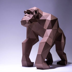 Peut inclure: Une sculpture en origami de gorille en papier brun debout sur une surface blanche. Le gorille est composé de nombreux petits triangles et a une apparence réaliste.