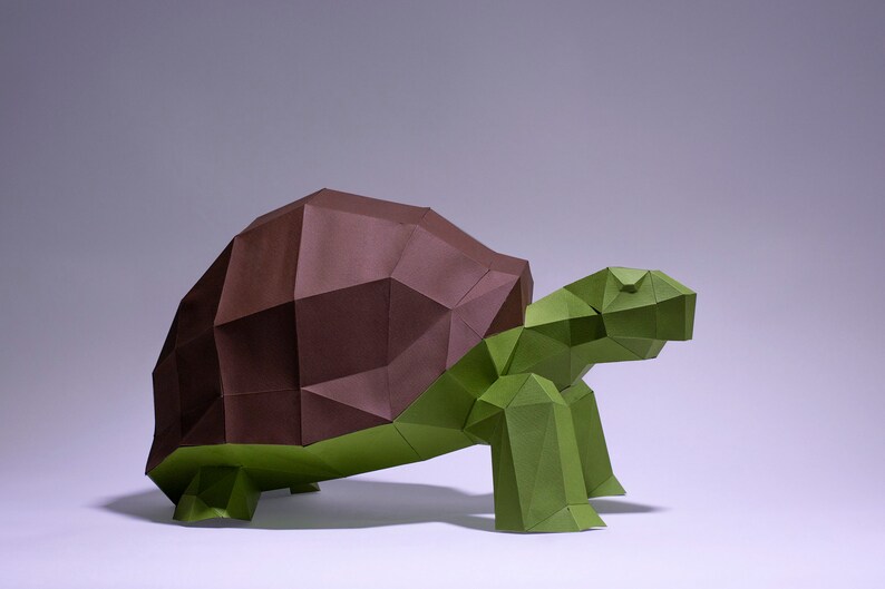 May include: An origami turtle sculpture made from brown and green paper. The turtle's shell is brown and its body and legs are green.