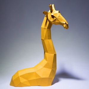 Op de afbeelding: Een gele origami-giraf-sculptuur met een geometrisch ontwerp. De giraf zit op een wit oppervlak.