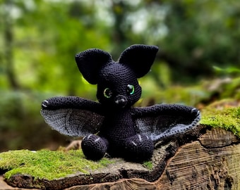 May include: A black crocheted bat with green eyes sitting on a tree stump covered in moss.