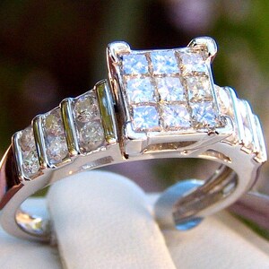 May include: A silver ring with a square-shaped center stone surrounded by smaller diamonds. The band is also set with diamonds.