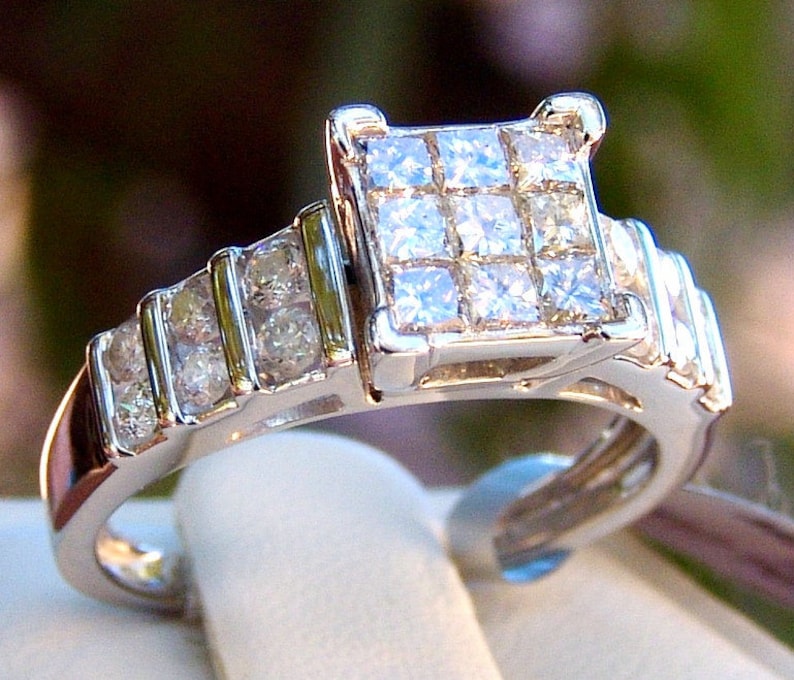 May include: A silver ring with a square-shaped center stone surrounded by smaller diamonds. The band is also set with diamonds.