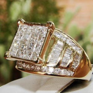 May include: A gold ring featuring a large square-shaped centre stone surrounded by smaller diamonds. The band is also set with diamonds in a baguette shape.