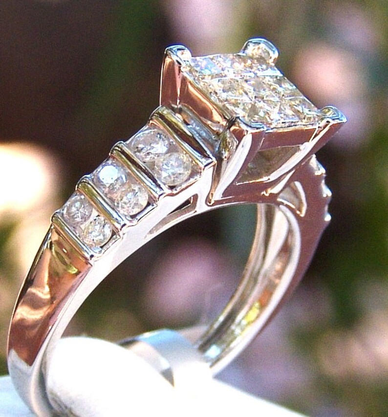 May include: A silver ring with a large square-shaped diamond in the center and smaller diamonds set in a band around the center stone.