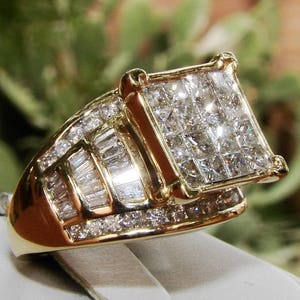 May include: A gold ring featuring a large square-shaped diamond centre stone surrounded by smaller diamonds. The ring is set in a gold band with a row of baguette-shaped diamonds.