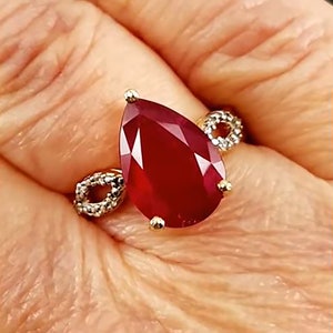 May include: A gold ring with a large, pear-shaped ruby gemstone and a smaller diamond band.