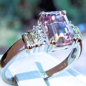 May include: A pink gemstone ring with a square emerald cut stone surrounded by smaller clear stones. The ring is set in silver.