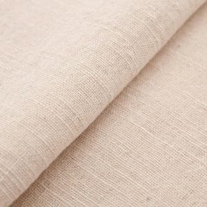 May include: Close-up of a folded piece of natural-colored linen fabric. The fabric has a coarse weave and a slightly textured surface. The color is a warm, neutral tone, with subtle variations in shade. The fabric appears soft and pliable.