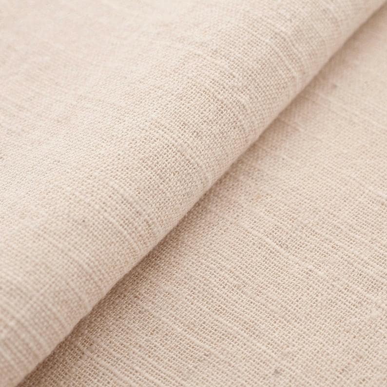 Puede incluir: Primer plano de un trozo de tela de lino de color natural doblado. La tela tiene un tejido grueso y una superficie ligeramente texturizada. El color es un tono c&aacute;lido y neutro, con sutiles variaciones de sombra. La tela parece suave y flexible.