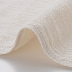 May include: Close-up of a white cotton fabric with a textured surface. The fabric is folded over, showing the edge of the material.