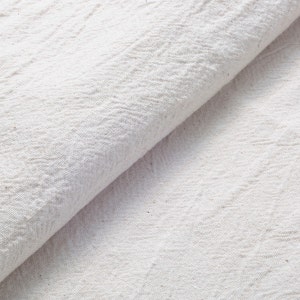 May include: Close-up of a white fabric with a textured surface. The fabric is folded in half, creating a diagonal line across the image.