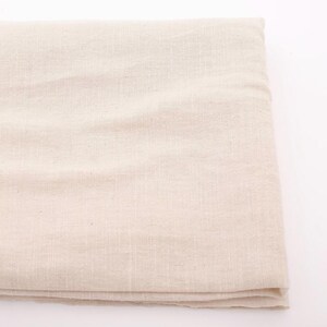 Puede incluir: Tela de lino beige doblada. La tela tiene una textura sutil y un color natural y neutro. El material parece ligero y adecuado para diversos proyectos textiles, como ropa o decoraci&oacute;n del hogar.