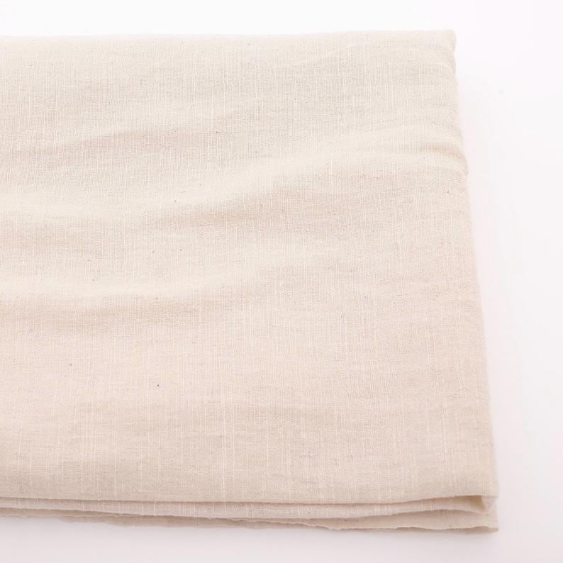 Puede incluir: Tela de lino beige doblada. La tela tiene una textura sutil y un color natural y neutro. El material parece ligero y adecuado para diversos proyectos textiles, como ropa o decoraci&oacute;n del hogar.