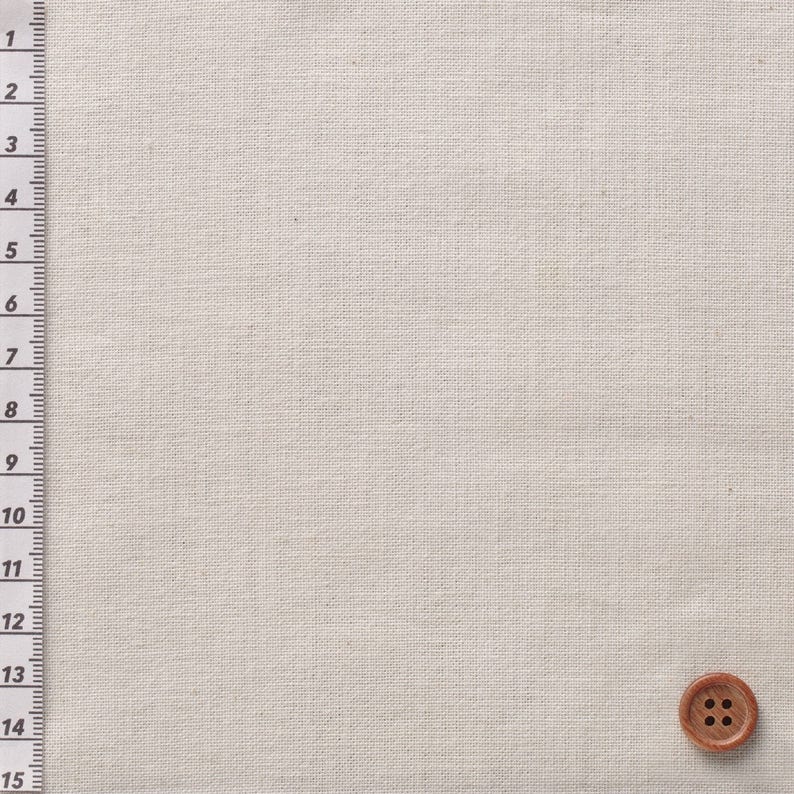 May include: A close-up of a beige fabric with a brown button in the bottom right corner. The fabric has a woven texture.