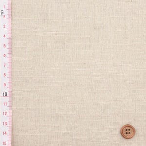 Puede incluir: Primer plano de tela de lino beige con un bot&oacute;n de madera. Una regla con medidas m&eacute;tricas est&aacute; a la izquierda. La tela tiene una textura sutil, ideal para costura.