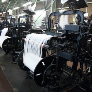 May include: A row of vintage industrial looms with spools of white thread, used for weaving fabric.