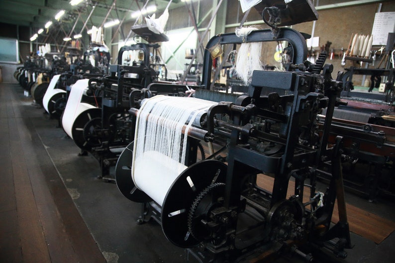 May include: A row of vintage industrial looms with spools of white thread, used for weaving fabric.