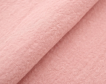 May include: Close-up of a soft, pink fabric with a textured weave. The fabric is folded in half, showing the texture and color.
