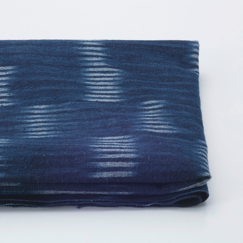 May include: A folded blue fabric with a white ikat pattern. The fabric has a soft, textured feel.