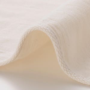 Puede incluir: Primer plano de una tela de algodón blanca con un borde cosido. La tela es suave y lisa, con una textura sutil.
