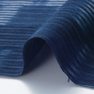 May include: Close-up of a dark blue fabric with a striped pattern. The fabric is folded over, showing the texture and weave.