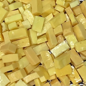 May include: A close-up of a pile of small, irregular, yellow glass tiles. The tiles are translucent and have a slightly iridescent sheen.