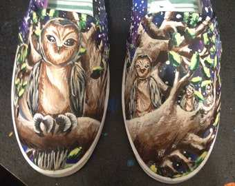 Könnte beinhalten: Ein Paar weiße Canvas-Schuhe mit einem Galaxie-Druck und handbemalten Eulen in einer Waldszene. Die Eulen sind braun, weiß und schwarz mit gelben Augen. Die Waldszene ist in Grün-, Braun- und Schwarztönen bemalt.