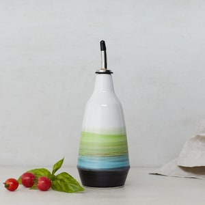 May include: A ceramic olive oil bottle with a black spout and a green, blue and black striped design.