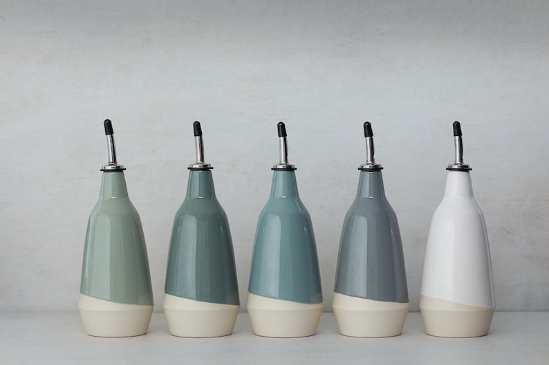 Op de afbeelding: Vijf keramische olie- en azijnflessen met een tweekleurige glazuur. De flessen zijn in tinten blauw en wit. De flessen hebben een tuit en een zwarte rubberen stop.