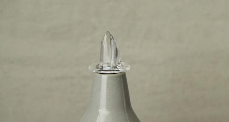 Op de afbeelding: Een glazen flesstopper van helder glas met een puntige bovenkant. De stopper is ontworpen om te passen op een fles met een smalle opening.