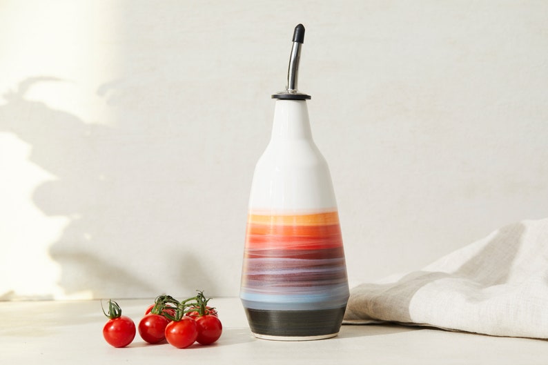 May include: A ceramic oil and vinegar bottle with a black and silver pour spout. The bottle is decorated with a colorful ombre design in shades of blue, purple, red, orange, and yellow.