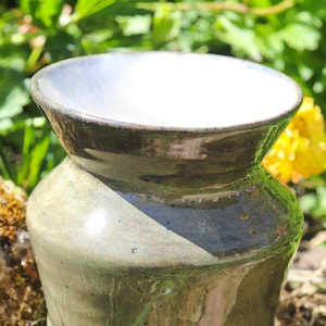 Può includere: Un vaso in ceramica fatto a mano con una parte superiore ampia e aperta e un corpo bulboso. Il vaso è smaltato in tonalità di verde e marrone, con un interno bianco. Il vaso è alto circa 15 cm.