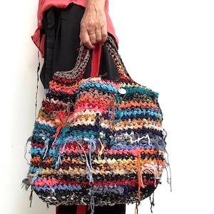 May include: A large, handmade tote bag with a colorful, textured design. The bag features a mix of vibrant colors including red, orange, blue, and black. The bag has a woven appearance with visible threads and a sturdy handle.