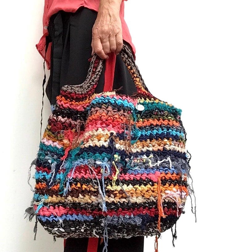May include: A large, handmade tote bag with a colorful, textured design. The bag features a mix of vibrant colors including red, orange, blue, and black. The bag has a woven appearance with visible threads and a sturdy handle.