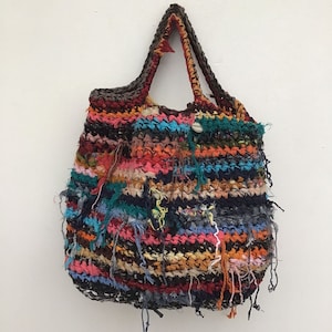 May include: A handmade tote bag with a colorful, textured design. The bag features a variety of colors, including red, blue, orange, and black, with frayed edges. The handles are a dark brown color.