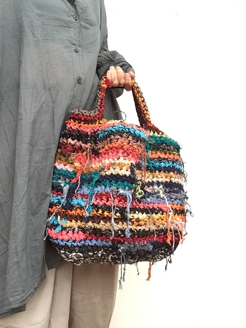 May include: A colorful, handmade tote bag with a textured, woven design. The bag features a mix of vibrant colors including red, blue, orange, and black. The handles are braided, and the bag has fringe details.