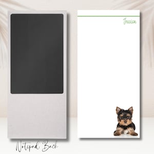 May include: A white notepad with a green line and the name "Jessi" written in green cursive. The back of the notepad is a light gray with a black rectangle and the text "Notepad Back". A small brown and black Yorkshire Terrier puppy is sitting on the notepad.