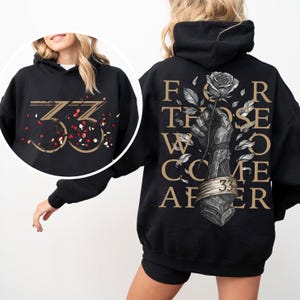May include: Black hoodie with gold text and graphics. The front features the number "33" with confetti. The back displays the words "FOR THOSE WHO COME AFTER" around a hand holding a rose. A ring with "33" is at the base of the rose.