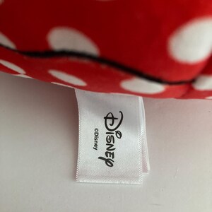 Op de afbeelding: Een close-up van rode stof met witte stippen. Een wit label met het Disney-logo en het woord "Disney" is aan de stof bevestigd. Het label bevat ook het copyrightsymbool.