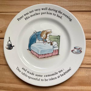 May include: White ceramic plate with a children's illustration. The plate shows a rabbit in bed being given tea by another rabbit. Text around the rim reads, "Peter was not very well during the evening. His mother put him to bed, and made some camomile tea: One table-spoonful to be taken at bed-time."