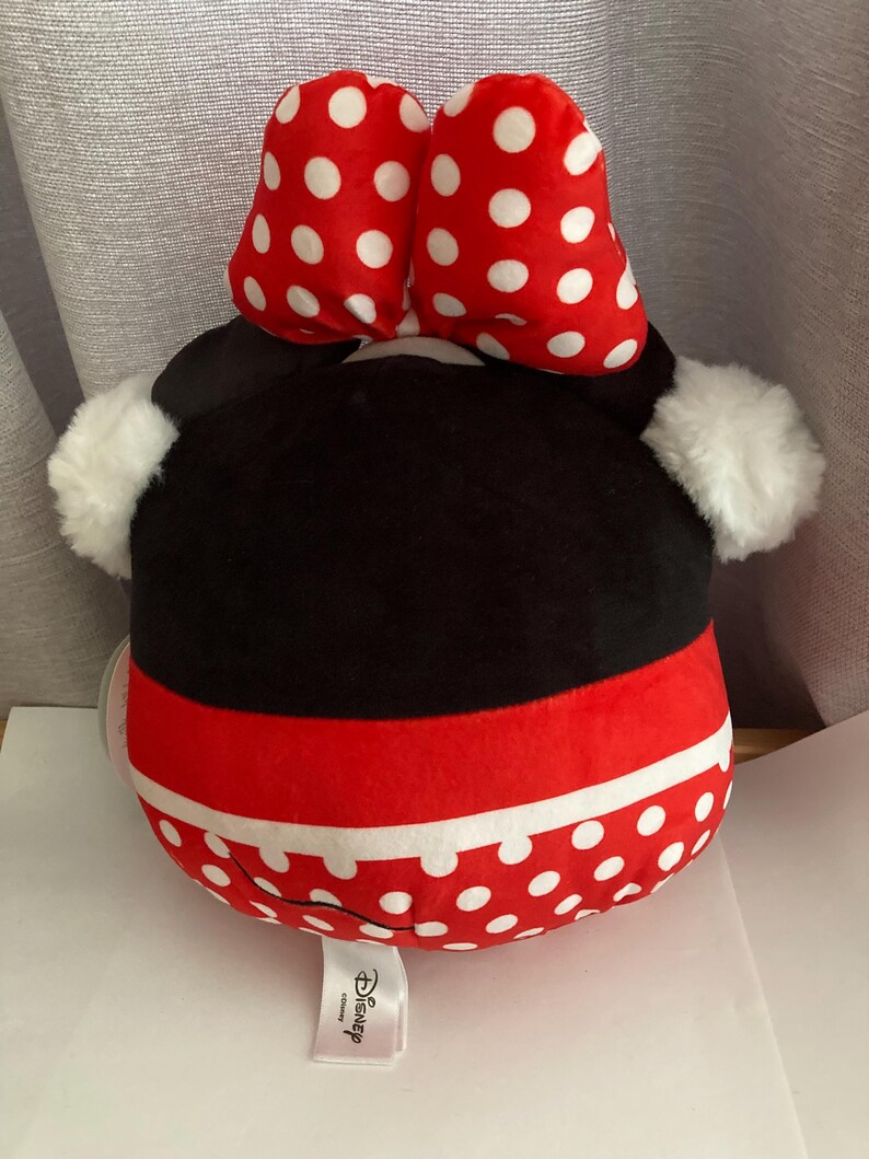 Op de afbeelding: Een Minnie Mouse knuffel met een rode en witte polka dot strik, zwarte kop en rode en witte polka dot rok. De knuffel heeft witte, pluizige oren en een Disney-label.