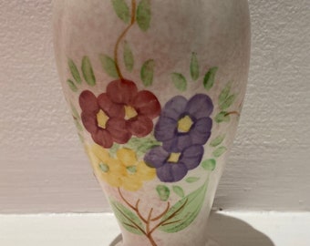 May include: A small, white ceramic vase with a floral design. The vase has a pink glaze and features painted flowers in shades of purple, red, yellow, and green.