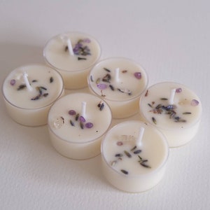 Puede incluir: Seis velas de t&eacute; blancas con lavanda y cristales morados incrustados en la cera. Las velas est&aacute;n dispuestas en c&iacute;rculo sobre una superficie blanca.