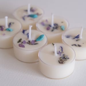 Puede incluir: Seis velas de t&eacute; blancas con flores secas y peque&ntilde;as piedras turquesa y moradas incrustadas.