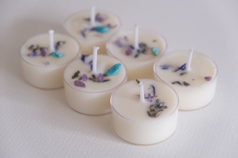 Puede incluir: Seis velas de t&eacute; blancas con flores secas y peque&ntilde;as piedras turquesa y moradas incrustadas.