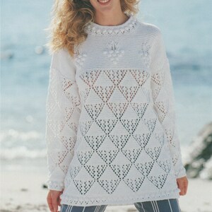 May include: White crocheted sweater with a lacy pattern and a round neckline. The sweater is loose fitting and has a slightly longer length. The model is wearing the sweater with blue and white striped pants.