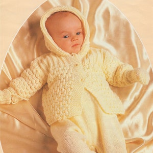 以下が含まれることがあります： 薄い黄色のニットのベビー服。フード付きジャケットと足付きのパンツがセットになっています。ジャケットはボタンで留めることができます。